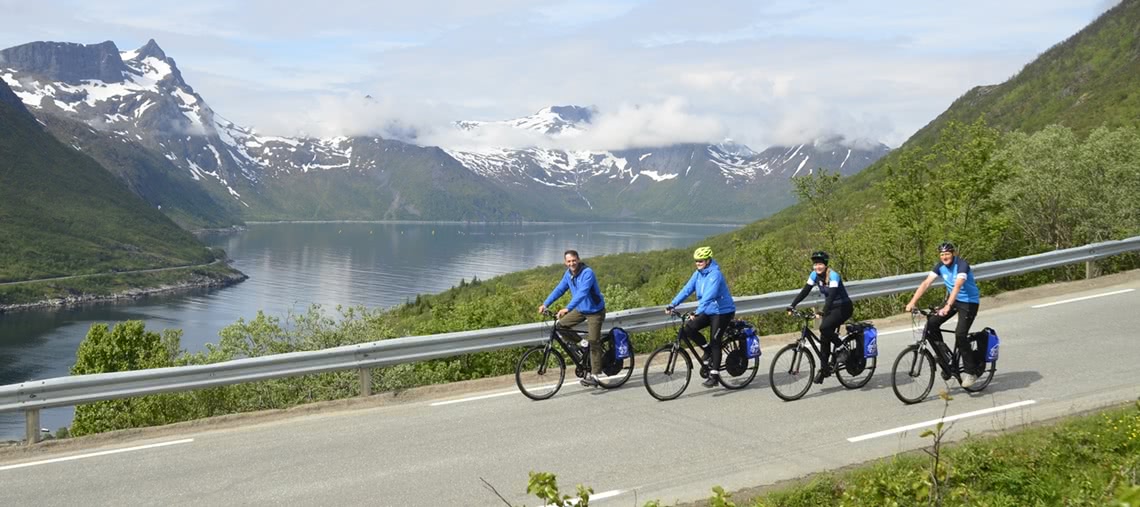 Radfahrer an norwegischem Fjord vor hohen Bergen